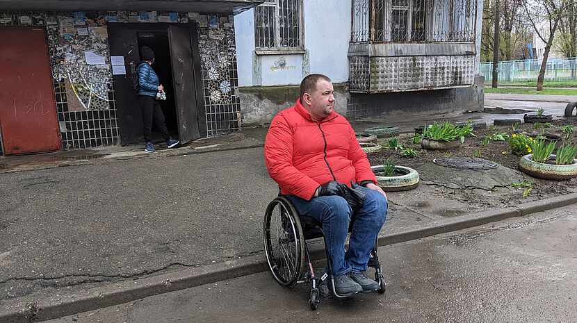 A man in a wheelchair is outside on the street in front of a building 