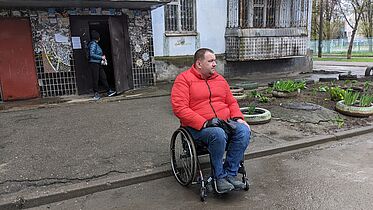 A man in a wheelchair is outside on the street in front of a building 